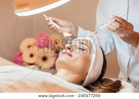 High-angle close-up view of the face of a beautiful woman during anti-aging facial massage with soft brushes in a modern cosmetic center