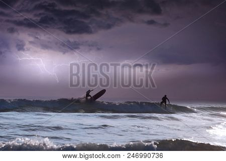 Silhouette of surfers on wave, stormy sky in the background