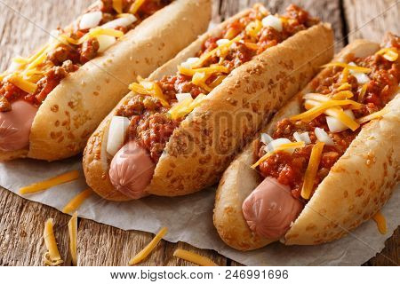 Authentic Chili Hot Dog With Cheddar Cheese, Onion And Spicy Sauce Close-up On Paper. Horizontal