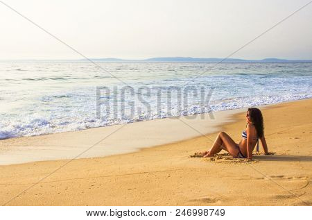 Single girl sitting in the golden sand by the sea shore in a summer day