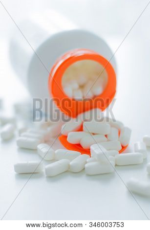 White Tablets Spilling Out Of A Plastic White Bottle With A Tablet