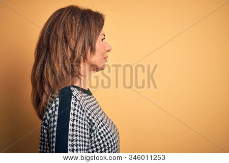 Middle age beautiful woman wearing casual sweater over isolated yellow background looking to side, relax profile pose with natural face with confident smile.