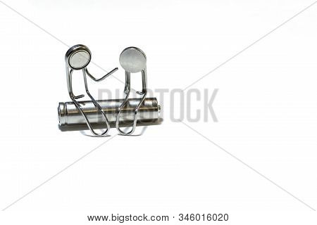 Two Paper Clips In The Form Of Men Sit On A Cylindrical Battery. The Faces Of The Little Men Are Mad
