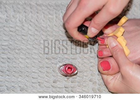 Closeup Of A Girl Taking Care Of Her Toenails, Painting With Red Lacquer, At Home, Against A Gray Ru