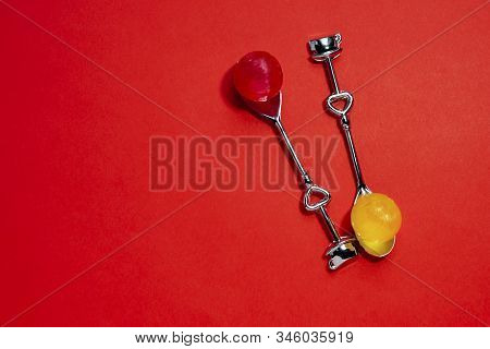 Two Stylish Metal Silver Teaspoons With Hearts And Round Candies On A Contrasting Red Background Wit