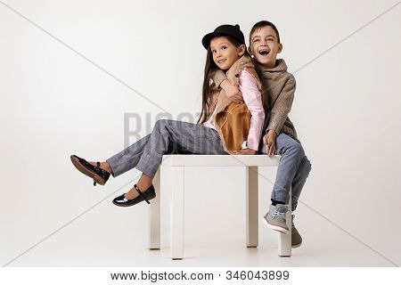 Cute Happy Stylish Little Couple Child Girl And Boy In Fashionable Clothes Sittting Together At Stud