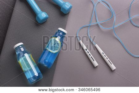 Sporty Background. Detox Isotonic Water With Lemon Slices And Gym Accessories On Gray Background