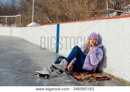 Lovely Young Woman Relaxing After Riding Ice Skates And Drinking Hot Drink From Termo Pot On The Ice