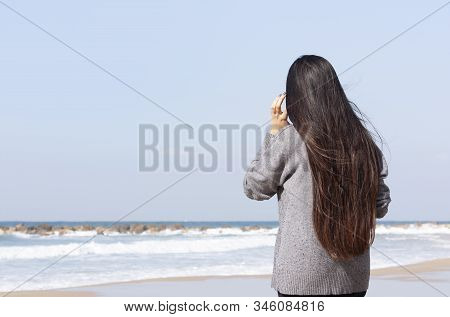A Girl With Long Dark Hair Stands Against The Sea