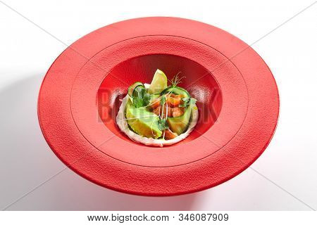Gourmet salmon tartar with avocado puree, fresh parsley, lemon, spices on red restaurant plate. Macro shot of delicious luxury raw trout, tuna or yellowfin tatar closeup