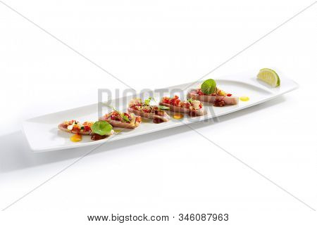 Appetizer with tuna tartar, seasonal vegetables and greens on white restaurant plate isolated. Macro photo of delicious healthy red fish tatar or tar-tar entree closeup
