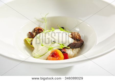 Risotto with grilled vegetables, carnaroli rice and cheese foam on white restaurant plate isolated. Traditional Italy rissoto or vegetable paella with cooked eggplants, mushrooms and greens closeup