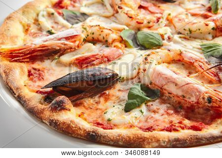 Italian seafood pizza with squid rings, mussels and shrimps on white restaurant plate isolated. Pizza ai frutti di mare topped with tomato sauce, basil and mozzarella closeup