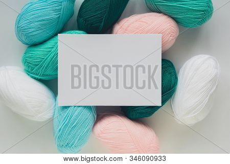 White Paper Sheet On Acrylic Soft Pastel Colored Wool Yarn Thread Skeins Heap On White Background, T
