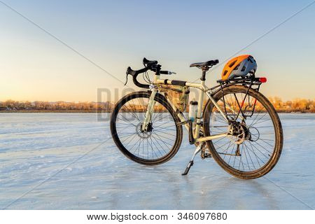 Winter biking, touring or commuting - bicycle on an icy lake. Helmet on racks, frame bag, kickstand. Riverbend Ponds Natural Area in Fort Collins, Colorado