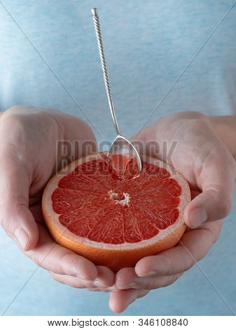 Closeup, Photo Of A Woman Holding Half Of Fresh Ripe Red Grapefruit In Her Hand. Blue Pastel Backgro