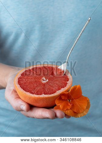Closeup, Photo Of A Woman Holding Half Of Fresh Ripe Red Grapefruit In Her Hand. Blue Pastel Backgro
