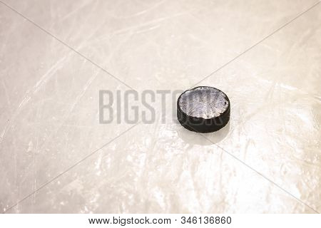Black Ice Hocikey Rubber Puck Located On Arena Ice Rink. Ice And Puck Have Small And Deep Scratches.