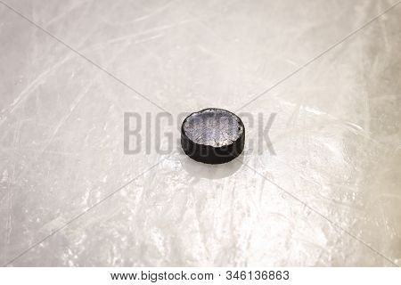Black Ice Hocikey Rubber Puck Located On Arena Ice Rink. Ice And Puck Have Small And Deep Scratches.