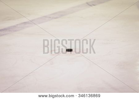 Black Ice Hocikey Rubber Puck Located On Arena Ice Rink. Ice And Puck Have Small And Deep Scratches.