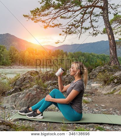 Blond Beautiful Girl Sitting On The Mat On The Stone Ground Drinking Coffee Or Tea, Resting After Sp
