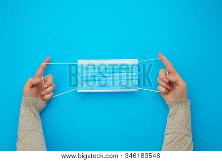 Female Hands Protracted Blue Sterile Textile Medical Mask With White Elastic Bands For Doctors On A 