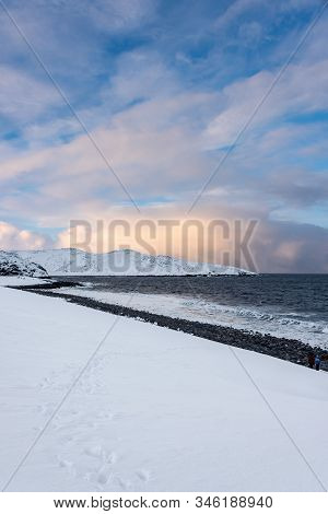 Footstep On A Snow Covered Beach Lead To The Sea Above The Arctic Circle With Two Small People (bott