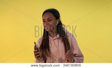 Cheerful African Girl Listening To The Music In Wireless Headphones On Yellow Background. She Is Mel