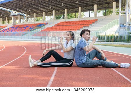 Portrait Of A Cute Hispanic Couple Drinking Water And Resting After Runnng On Track At Studium, Heal