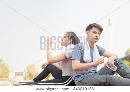Portrait Of A Cute Hispanic Couple Drinking Water And Resting After Runnng On Track At Studium, Heal