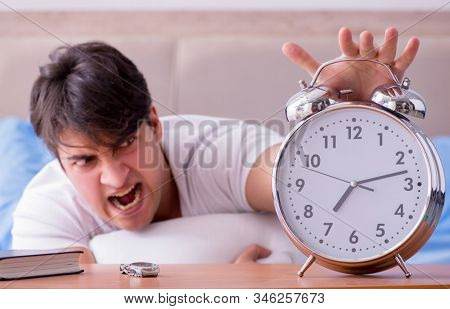 Man in bed frustrated suffering from insomnia with an alarm cloc