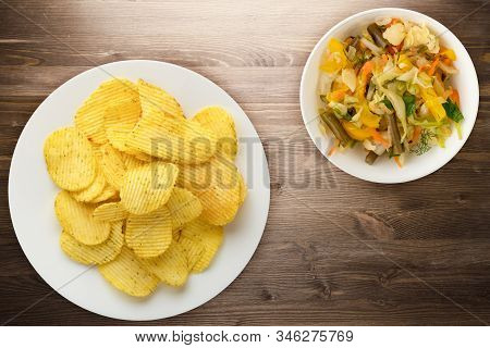 Potato Chips On A White Plate With Vegetarion Salad. Chips On A Brown Wooden Background Top View.