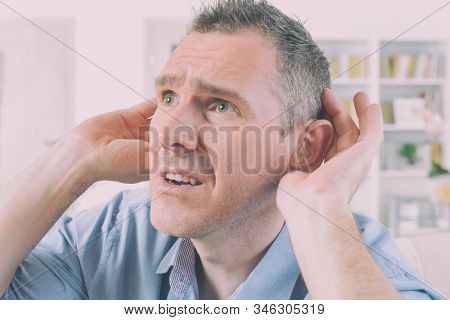 Man wearing deaf aid in ear attempting to hear something