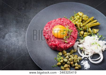 Gourmet tartar raw from beef fillet with yellow of the egg and gherkin with capers and onion rings as closeup on modern design plate with copy space