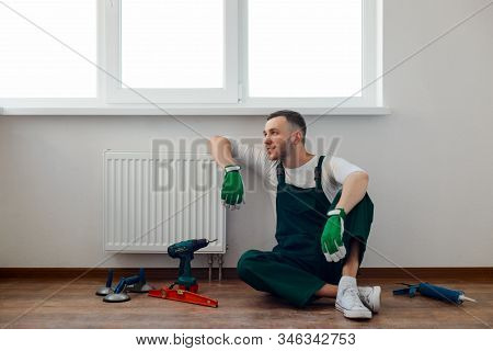Handyman Is Resting After Work, Leant On A Heater And Sitting On The Floor
