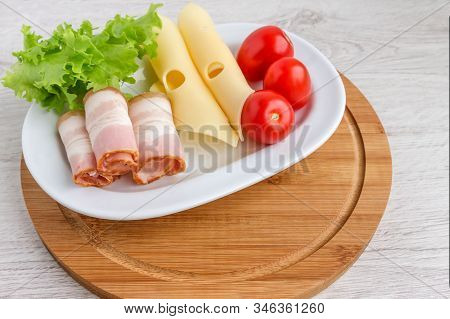 On A White Dish Are Fresh And Tasty Products For A Quick Snack-cheese,bacon,tomatoes And Greens