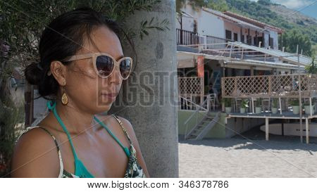 Woman With Sunglasses Sitting With Beach Restaurant In The Background In Eressos, Lesvos, Greece