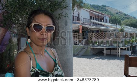 Woman With Sunglasses Sitting With Beach Restaurant In The Background In Eressos, Lesvos, Greece