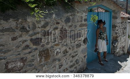 Asian Woman In Sunglasses And Hat Standing In Front Of Traditional Greek House In Village Of Eressos