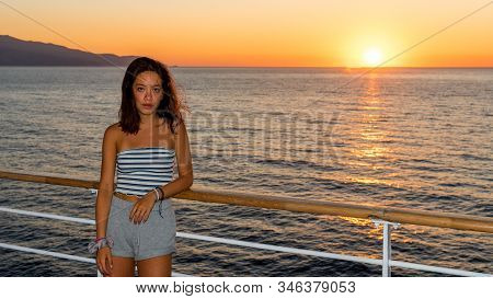 Asian Teen In Tube Top Standing On Deck Of Ferry Looking Away From Sunset On Ferry To Greece