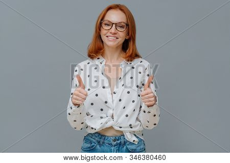Positive Redhaired Woman With Gentle Smiles Shows Thumbs Up, Demonstrates Like Or Approval Gesture, 
