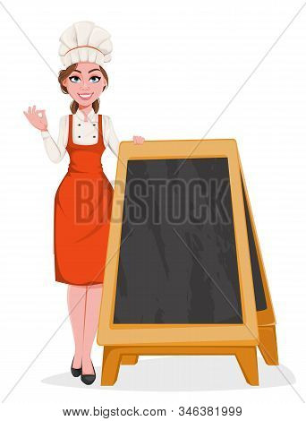 Beautiful Young Chef Woman Standing Near Blank Menu Blackboard. Pretty Cook Lady In Professional Apr