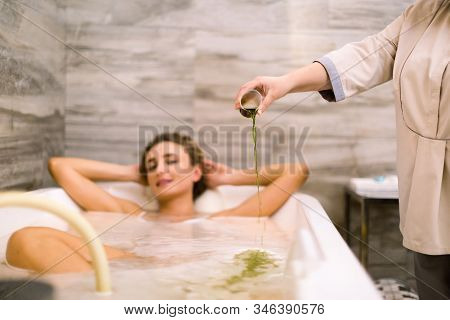 Front View Of Young Woman In Bath During Hydromassage In Beauty Salon. Woman Therapist Fills The Bat