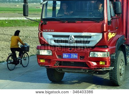 North Korea - May 5, 2019: Traffic On A Countryside Road. The Red Heavy Truck Carrying A Container O