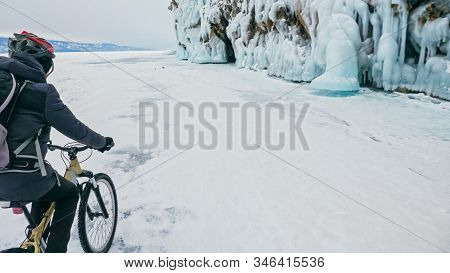Man Is Riding Bicycle Near Ice Grotto. Rock With Ice Caves Icicl