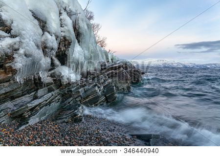 Icicles Hanging From The Rocks On The Shore Tornetrask, Sweden. Beautiful Waves. Long Shutter Speed