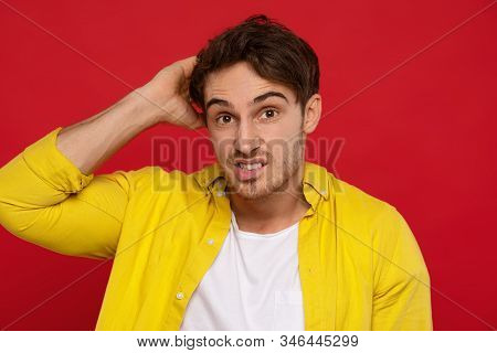 I Know Nothing. Uncertain Handsome Man In Yellow Shirt Scratching His Head Isolated On Red Backgroun