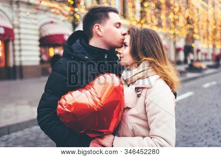 Loving Guy On The Street Kisses A Girl On The Forehead On A New Years Background In The Afternoon. .