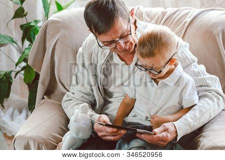 Elderly Grandfather And His Little Grandson Use A Tablet Device
