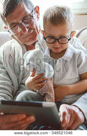 Elderly Grandfather And His Little Grandson Use A Tablet Device